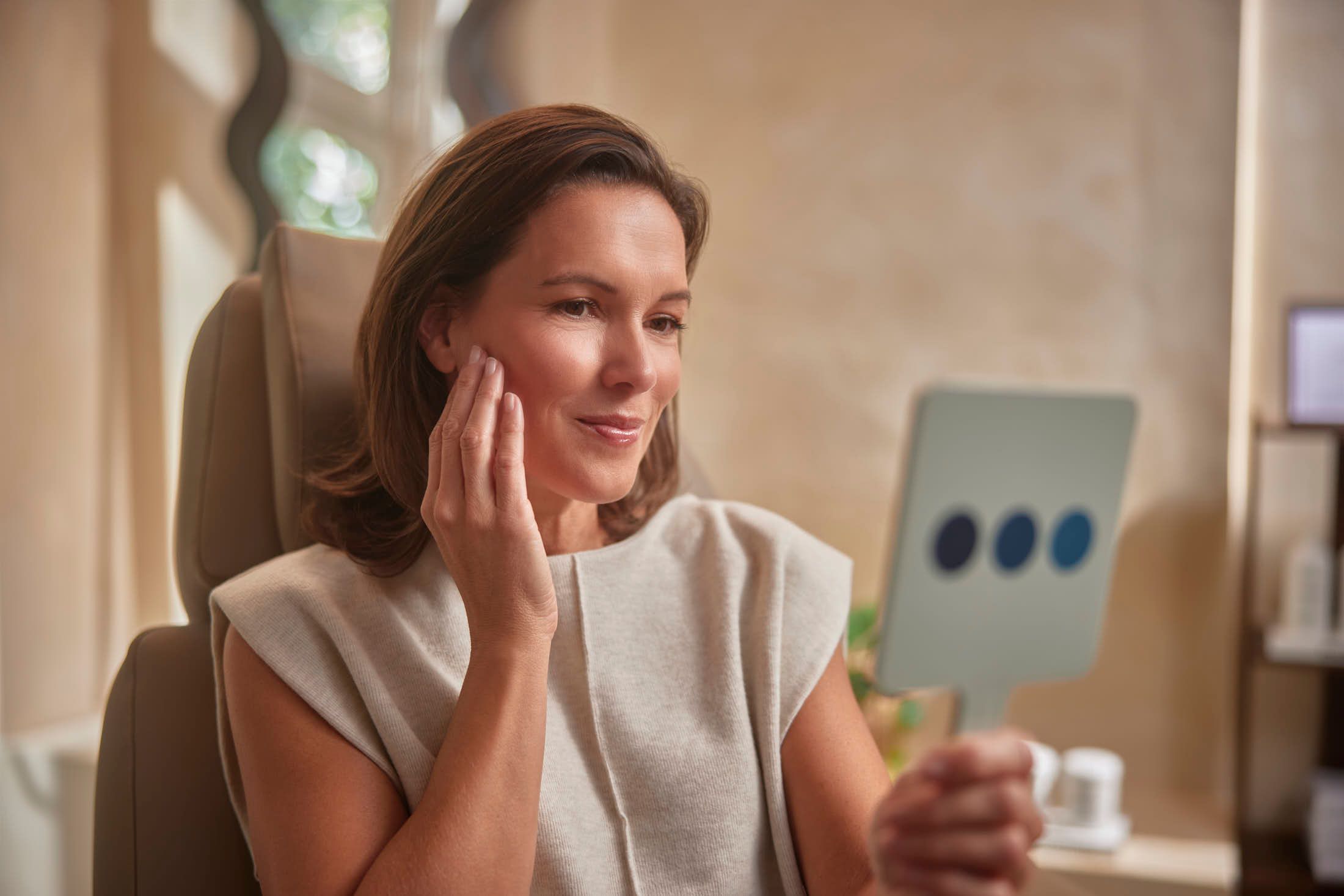 Client bekijkt haar kaaklijn en hals in spiegel voor NeckTite behandeling bij The Body Clinic