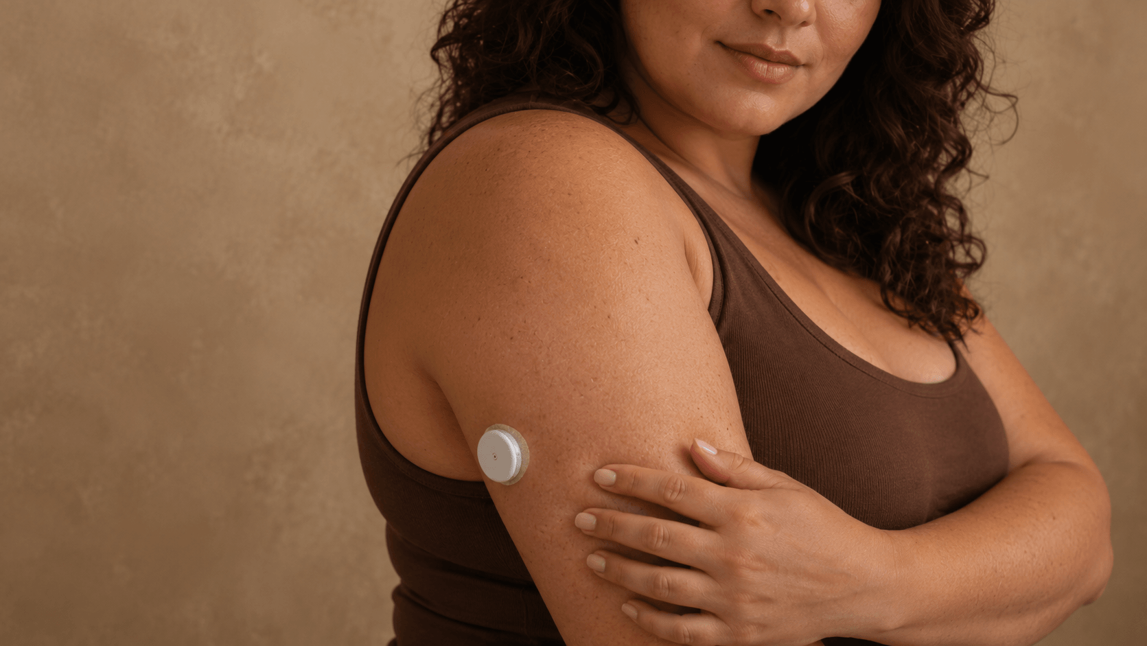 Woman with a continuous glucose monitor on her upper arm, wearing a brown top.