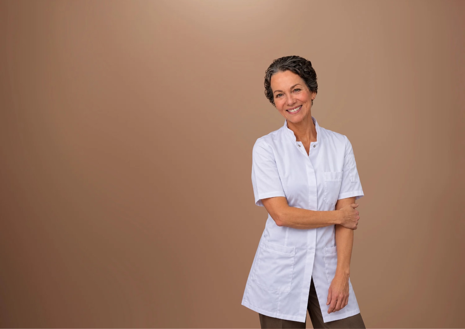 Smiling woman in a white tunic against a plain brown background.